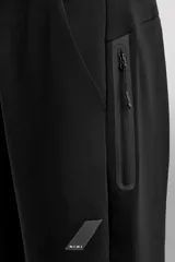 Pantalón jogger color marrón oscuro, corte regular fit, confeccionado en tejido técnico compacto de algodón con elasticidad. Cuenta con cintura elástica ajustable con cordón, bolsillos frontales y bolsillo lateral con cierre de cremallera.