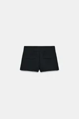 Shorts de tiro medio color negro, con bolsillos delanteros y falsos bolsillos con solapa en la parte trasera. Cierre frontal con cremallera y ganchos metálicos.
