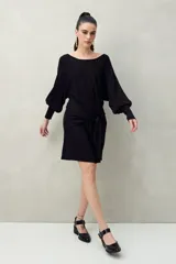 Vestido corto negro de punto con brillo sutil, mangas largas amplias, falda ajustada y lazo frontal en la cintura.