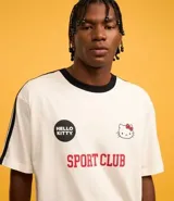 Remera blanca de corte boxy con cuello redondo y detalles en negro. Estampado frontal con logo de Hello Kitty y texto "Sport Club".