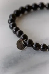Pulsera elástica de piedras naturales color marrón con dije circular dorado con la palabra "AIRE" grabada.
