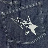 Pantalón de jean azul oscuro, corte ultra baggy, con costuras blancas a contraste y un rayo bordado en el bolsillo lateral.