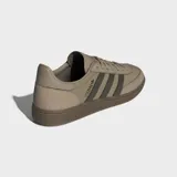 Zapatillas Adidas Handball Spezial de corte bajo, con parte superior de ante en tono beige claro y tres franjas laterales en verde oliva. Presentan puntera en T y suela de goma color café. La inscripción "SPEZIAL" se encuentra en el lateral en color oscuro.