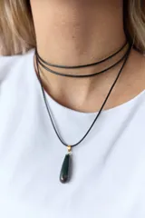 Gargantilla con tres tiras de cuero negro y dije en forma de gota de piedra natural verde y marrón con engarce de acero quirúrgico dorado.
