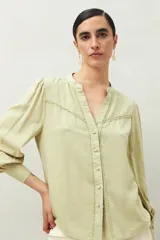 Camisa celeste de manga larga con cuello redondo y escote en V. Presenta detalles de pasamanería en el frente y las mangas, y botones forrados al tono. De corte fluido.