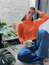 Polera de punto color naranja, con cuello alto y diseño trenzado.