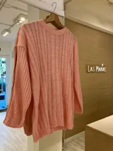 Sweater tejido color salmón con cuello redondo, diseño de ochos en el frente y rayas horizontales en las mangas largas.