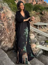 Vestido largo negro con estampado de jungla con palmeras, jirafas y leopardos. Tiene breteles finos, escote en V cruzado y cinturón con apliques brillantes.