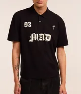 Remera boxy de mangas cortas, confeccionada en algodón, color negro, con cuello polo y lettering "93 MAD" y una cruz estampada en la parte delantera.