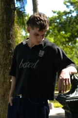 Chomba negra de corte cuadrado con cuello polo y mangas cortas. Presenta un escudo estampado en el pecho con diseño de fútbol retro y la palabra 'boxed' estampada en el frente.