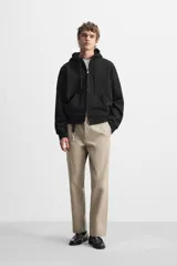 Pantalón chino color verde militar, de corte recto, con bolsillos laterales y traseros de vivo. Cierre frontal con cremallera y botón.