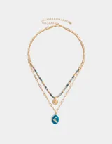 Collar corto dorado de doble cadena, una de eslabones y otra de cuentas de colores. Incluye un dije dorado con forma de sol y un dije azul con una figura grabada.
