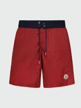 Short de baño rojo con cintura elástica azul marino y cordón de ajuste con ojales metálicos. Presenta el logo circular de Moncler bordado en la pierna izquierda.