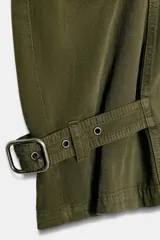Pantalón cargo de mujer color verde militar, tiro medio, corte ancho y recto (barrel). Presenta bolsillos laterales y bolsillos de plastrón con solapa en las piernas. El bajo es ajustable con trabillas y hebillas metálicas.