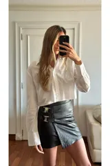 Minifalda negra de cuero sintético con corte irregular y detalle de hebillas decorativas en el lateral.