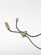 Collar con cordón largo ajustable de poliéster negro. Presenta un dije metálico de forma orgánica con acabado dorado, que contiene un aplique central de resina blanca con apariencia de perla irregular.