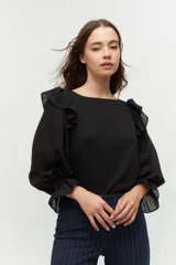 Blusa negra con escote bote y mangas largas abullonadas con puños ajustados. Presenta volados en los hombros.