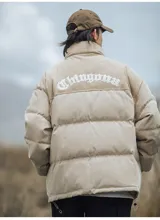 Campera puffer marrón con paneles horizontales acolchados. La parte superior de la espalda es de pana marrón con el texto 'Chingona' bordado en blanco. Posee cordón ajustable en el ruedo y se lleva superpuesta a una sudadera con capucha gris.