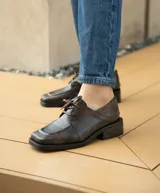 Zapato acordonado de cuero vacuno color marrón oscuro, con suela de goma, horma cuadrada y tacón bajo.