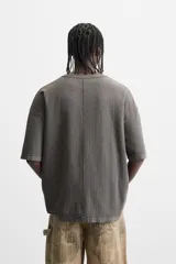 Camiseta color gris verdoso de punto tejido en hilatura de algodón, con cuello redondo, manga corta, efecto lavado y acabados irregulares.