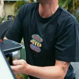 Remera negra de manga corta con estampa centrada en el pecho con el logo de la marca en colores verde, naranja y violeta.