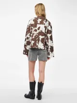 Chaqueta de jean con estampado animal print de vaca en tonos marrones y blancos, corte recto, cuello camisero y cierre frontal con botones.