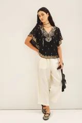 Blusa de gasa traslúcida negra con escote en V y mangas amplias de largo irregular, bordada con canutillos, lentejuelas y mostacillas doradas. Incluye gancho oculto en el escote y viso al tono con breteles regulables y puntilla en el escote.