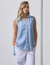 Camisa celeste sin mangas de lino con cuello clásico, cierre frontal con botones, dos bolsillos con solapa en el pecho y corte asimétrico.