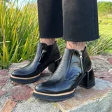 Botas cortas de cuero negro con textura de piel de serpiente, cierre lateral con cremallera, taco de madera forrado en cuero y punta fina.