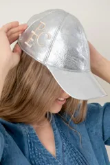Gorra tipo baseball de cuero ovino italiano color plateado metalizado, con visera a tono. Presenta un bordado de monograma en color beige claro en el lateral frontal.