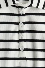 Remera polo de manga corta con cuello clásico y tapeta de botones. Diseño a rayas horizontales en blanco y negro, de corte entallado y tejido acanalado.