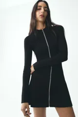 Vestido corto negro de punto con cuello redondo y manga larga. Presenta cierre frontal con cremallera metálica.