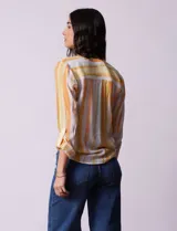 Blusa de gasa estampada a rayas verticales en tonos celeste, lila, naranja y marrón. Tiene cuello a la base con escote en V y botones. Delantera con bolsillo aplicado. Largo de manga regulable con presilla y botón. Terminación anudada opcional.
