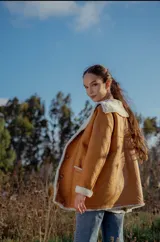 Campera gamulan color camel de cuero italiano con interior de piel sintética blanca. Tiene cuello solapa amplio, cierre con botones y bolsillos laterales.