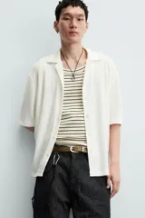 Camisa de manga corta con cuello bowling y calce relajado. Presenta un tejido con textura estructurada y efecto lavado, con cierre frontal de botones al tono.