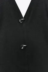 Minivestido negro con forma de chaleco, cuello halter, escote en pico, botones metálicos y bajo globo.