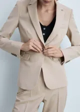 Blazer color beige con cuello de pico con solapa, hombros estructurados, cierre de botón en la parte delantera y dos bolsillos de ribete en la parte delantera.