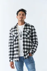 Sobrecamisa de algodón para hombre con interior de corderito, estampado a cuadros en tonos negro, blanco y azul. Tiene cierre de botones, bolsillos tipo cartera y logo en goma. El modelo usa talle M.