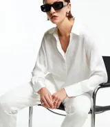 Camisa blanca de satén con cuello inglés, manga larga y cierre frontal con botones.
