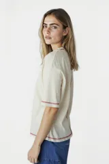 Remera beige de corte holgado con cuello redondo y mangas cortas. Presenta un pequeño estampado de un sol azul en el centro del pecho y costuras en color rojo en cuello, mangas y ruedo.