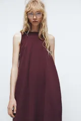 Vestido midi negro de cuello redondo y sin mangas. Corte amplio y fluido, con bolsillos laterales ocultos y cierre trasero con cremallera invisible.
