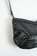 Cartera negra con correa corta para el hombro y tachas plateadas.