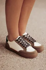 Zapatillas urbanas de cuero ecológico blanco con puntera y talón de gamuza sintética color beige. Cordones negros y suela de goma color caramelo.