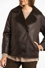 Chaqueta tipo gamulán de calce oversize en color marrón oscuro, con exterior de poliéster y forro de corderito sintético. Presenta cuello de solapa ancha y cierre frontal con botones.