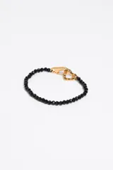 Pulsera de cuentas facetadas negras con cierre de mosquetón dorado y dije de corazón con logo grabado.