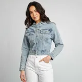 Chaqueta de jean celeste de corte cropped, con cuello clásico, cierre frontal con botones metálicos, bolsillos de parche con solapa en el pecho y mangas largas con puños abotonados.