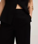 Pantalón de mujer modelo pantalona Wide Leg color negro, confeccionado en tejido flame (viscosa y poliéster). Presenta trabillas en la cintura, cierre tradicional y frisos laterales.