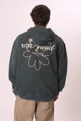 Sudadera con capucha de color verde oscuro (o verde petróleo) con efecto lavado, corte holgado y bolsillo canguro. Presenta un pequeño bordado blanco en el pecho con un diseño floral y texto.