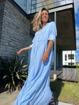 Vestido camisero largo celeste con rayas verticales blancas, cuello camisero, manga larga con puño y abotonadura frontal. Diseño escalonado con volantes en cada corte.