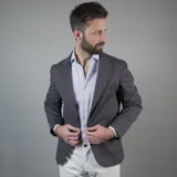Saco color beige de gabardina, con solapas de muesca, cierre de dos botones, tres bolsillos externos y un bolsillo interno.